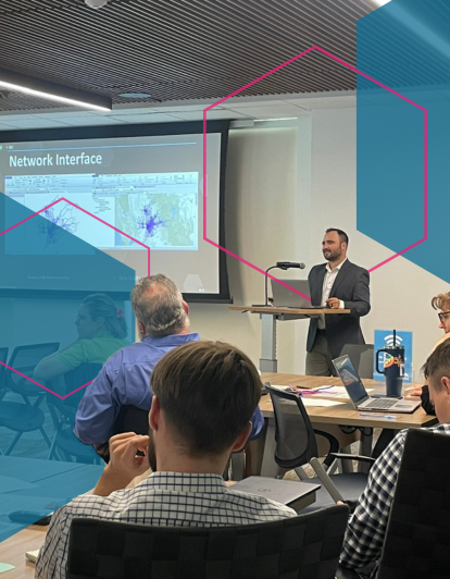 Man at podium presenting to group and background with colorful hexagons
