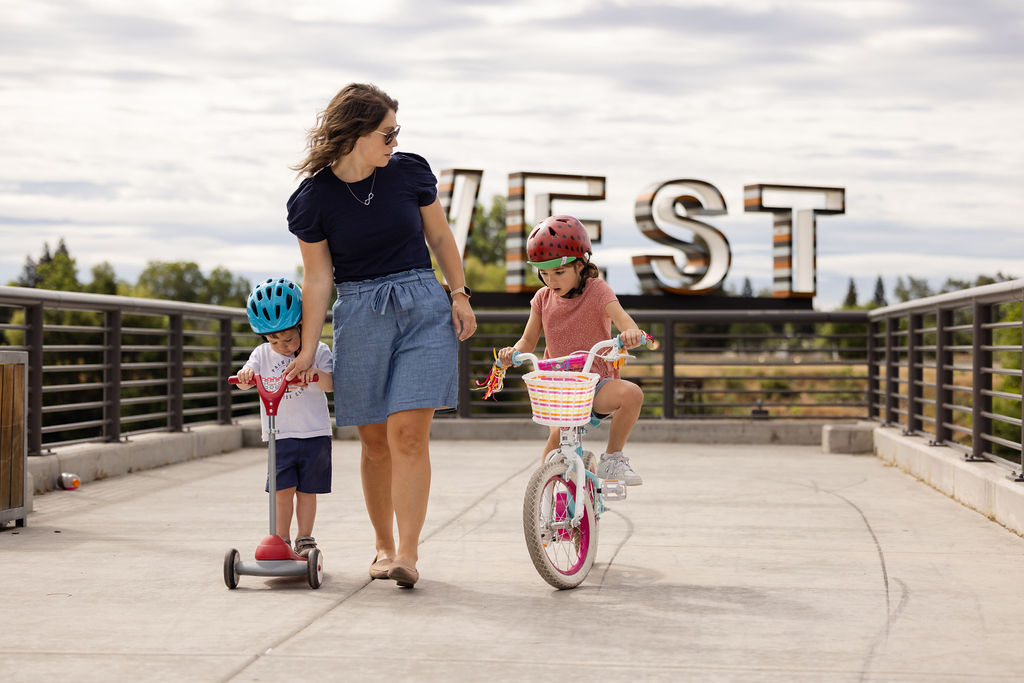 Woman guiding child on a bike and another child on a scooter