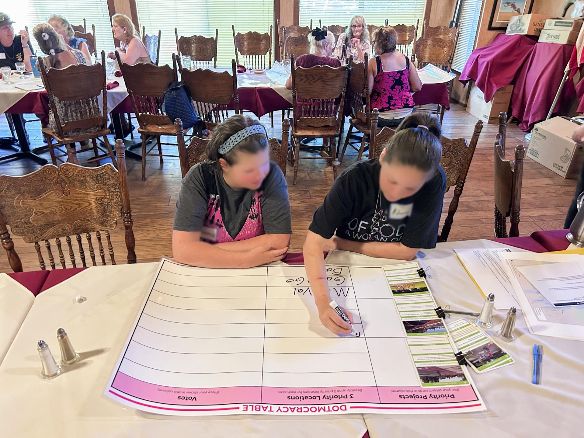 Two people sitting at a table writing comments on a poster sized piece of paper