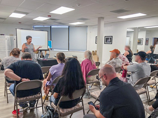 Backs of group of people sitting and listening to a presenter at the front of the room