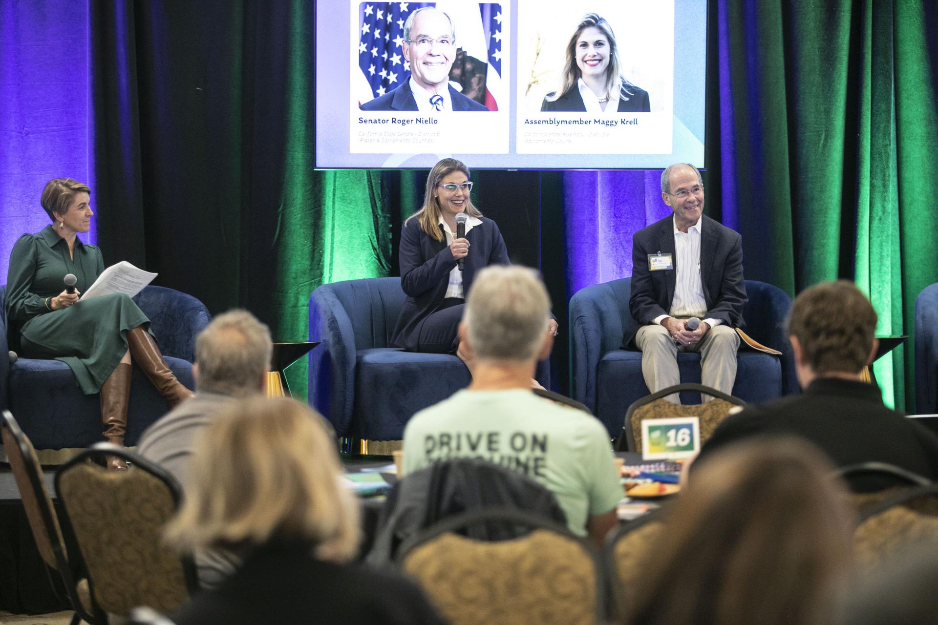 Three people sitting on stage presenting to audience