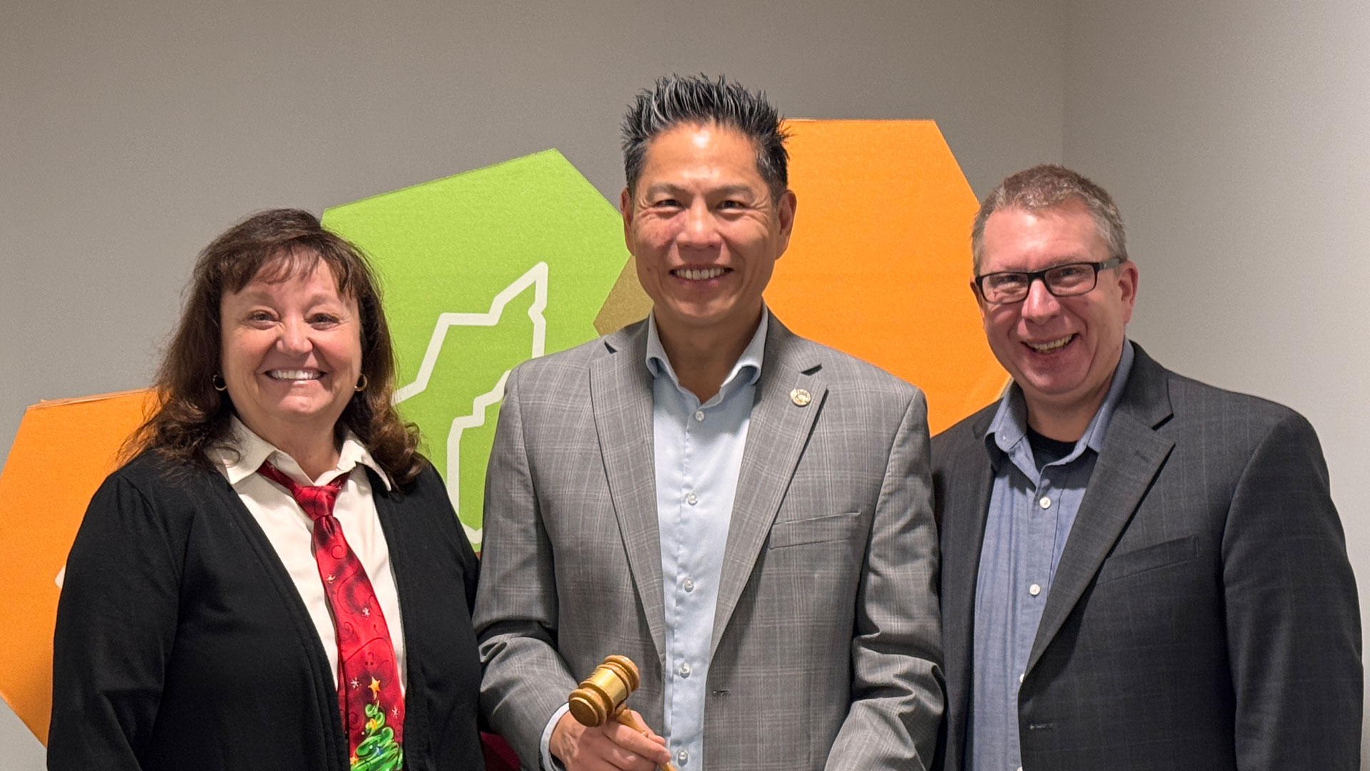 Directors Gayaldo, Suen, and Bradford posing for photo inside in front of region mark display