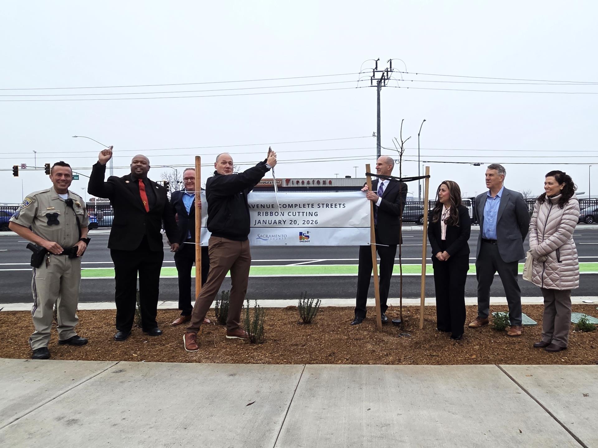 Group of six people standing in a line while Desmond cuts the ribbon in the center of the group