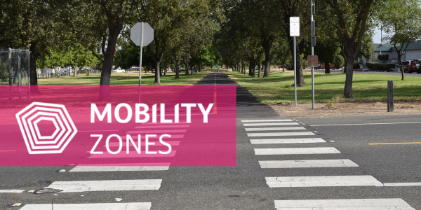 looking down trail and cross walk with green grass on both sides. mobility zones logo overlayed on image
